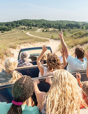 people raise their hands high while riding in dune vehicle