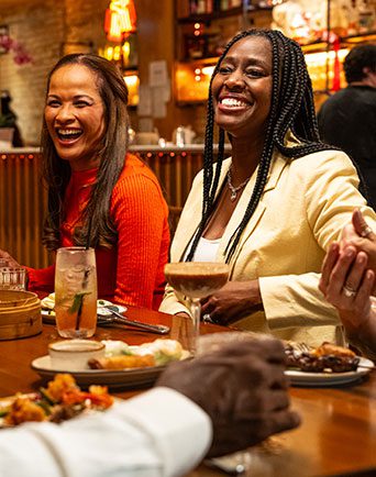 Women smile at a table filled with drinks and food