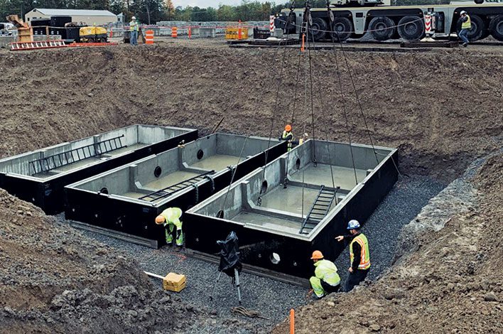 Multiple precast tanks are being connected in a field.