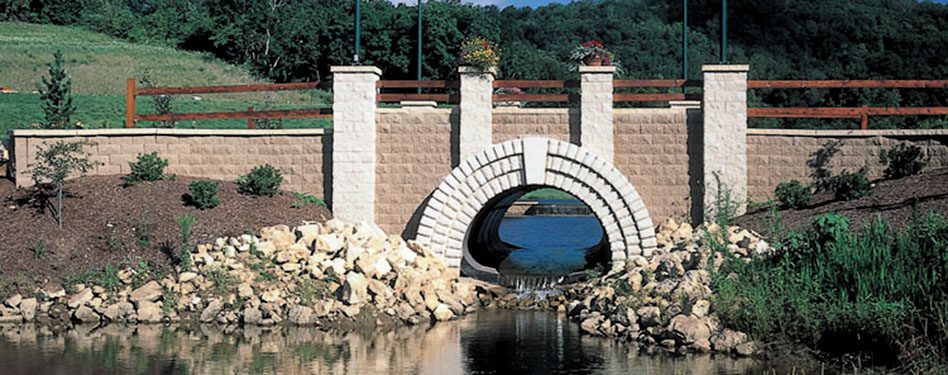 A precast concrete bridges surrounding by lush landscaping spans a culvert.