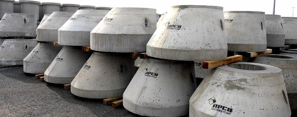 Manhole risers with the NPCA Certified Plant logo painted on them are stacked in a product yard.