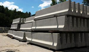 Highway barriers are stack three-high in a precast concrete plant yard.