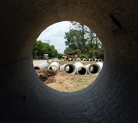Seen from inside a precast concrete pipe, other pipes rest at a project site.
