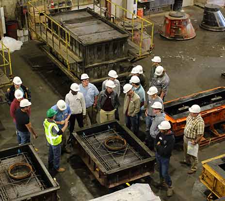 Visitors to a precast plant gather around a form as a worker explains how the plant uses the form.