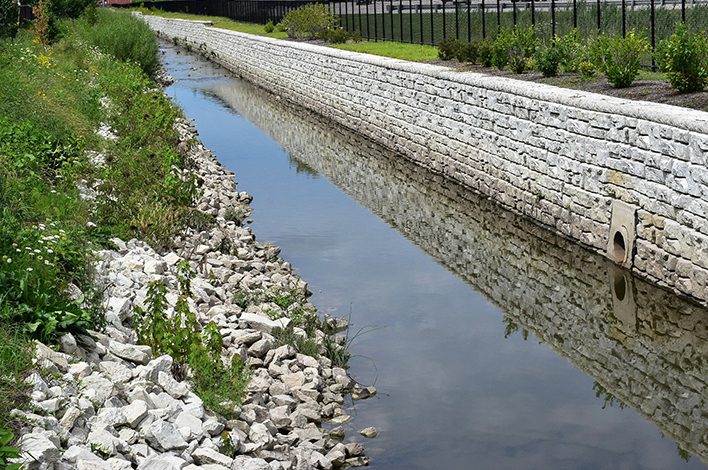 A fully constructed precast wall stretches the length of a ditch with shallow water.