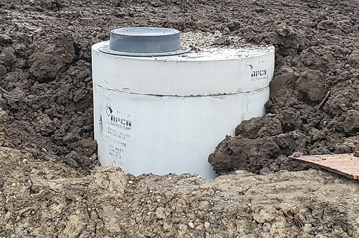 A round, concrete wet well sits in the ground.