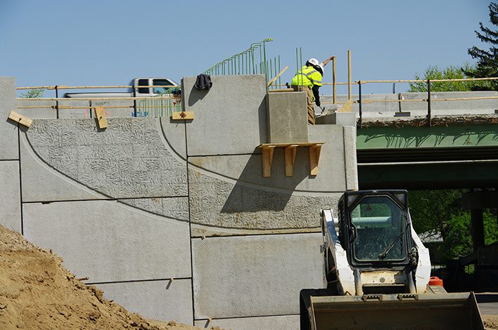 Two men work on top of a bridge installing wall panels.