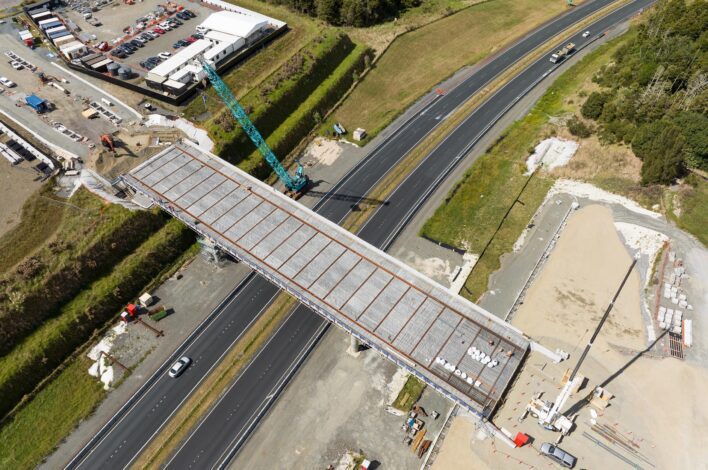 Aerial image of a precast concrete bridge piece being placed over a highway.
