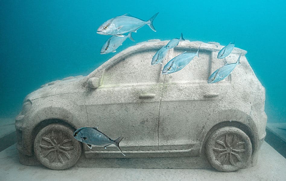 Marine-grade concrete car sculpture underwater with fish swimming around it