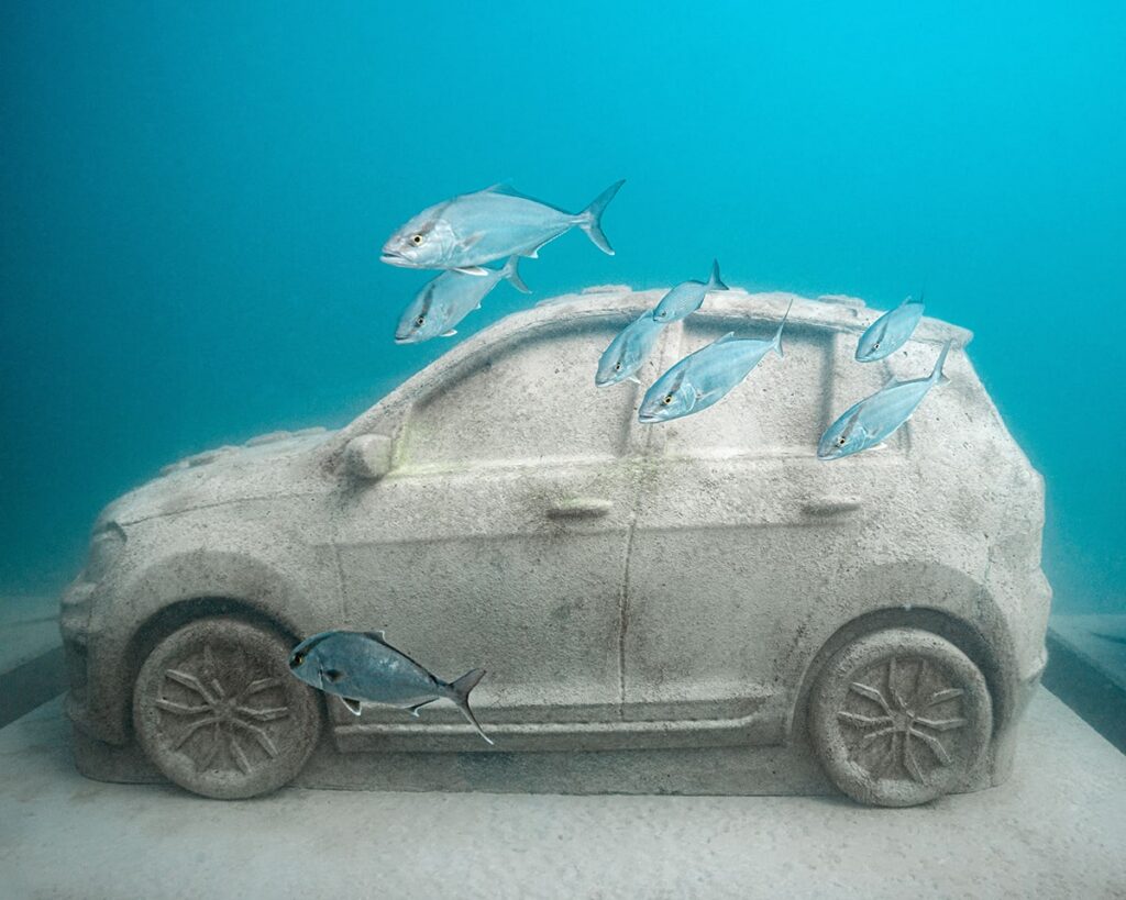 Marine-grade concrete car sculpture underwater with fish swimming around it